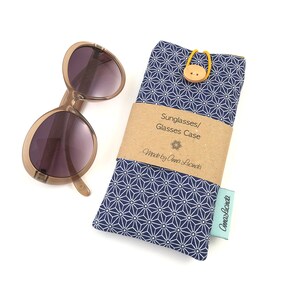 May include: A navy blue fabric sunglasses case with a white geometric pattern. The case has a brown button closure and a label that reads "Sunglasses/Glasses Case Made by Anna Lucinda".