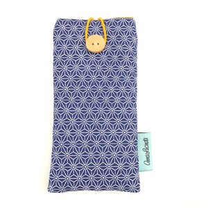 May include: A blue and white geometric patterned glasses case with a yellow elastic closure and a brown button. The case has a light blue label with the text "Cami & Lucinda" printed on it.