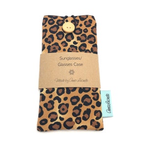 May include: A brown and black leopard print glasses case with a wooden button closure. The case has a brown paper label that says "Sunglasses/Glasses Case" and "Made by Anna Lucinda".