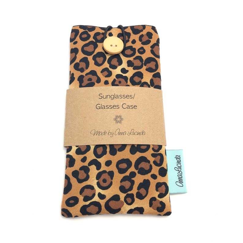 May include: A brown and black leopard print glasses case with a wooden button closure. The case has a brown paper label that says "Sunglasses/Glasses Case" and "Made by Anna Lucinda".