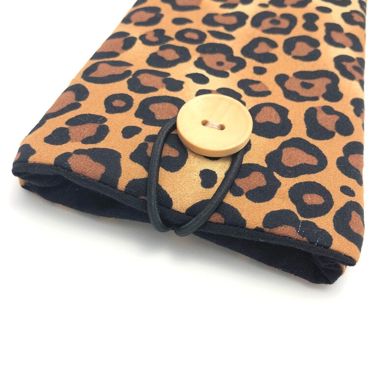 May include: A brown and black leopard print fabric pouch with a wooden button closure and a black elastic strap.