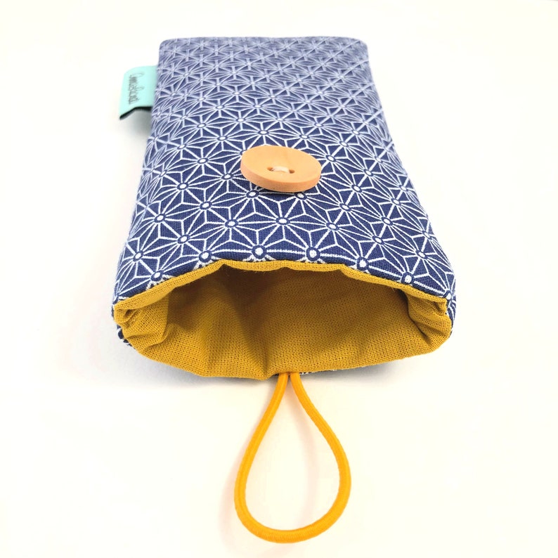 May include: A blue and white geometric patterned pouch with a yellow lining and a brown button closure. The pouch has a yellow elastic loop for carrying.