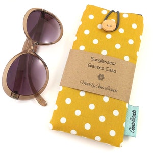 May include: Yellow polka dot fabric sunglasses case with a brown button closure and a label that reads "Sunglasses/Glasses Case Made by Anna Lucinda".