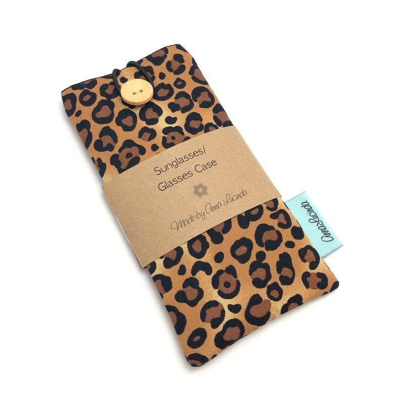 May include: A brown and black leopard print glasses case with a wooden button closure. The case has a brown paper label that says "Sunglasses/Glasses Case" and "Made by Anna Lucinda".