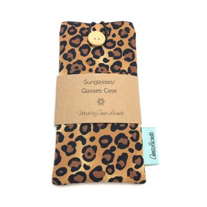 May include: A brown and black leopard print glasses case with a wooden button closure. The case has a brown paper label that says "Sunglasses/Glasses Case" and "Made by Anna Lucinda".