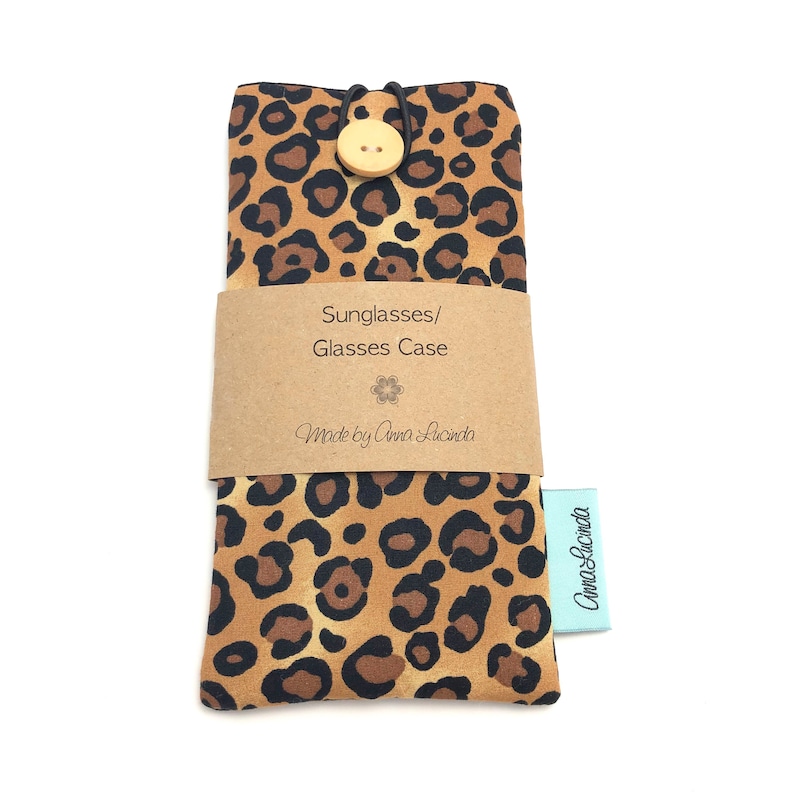 May include: A brown and black leopard print glasses case with a wooden button closure. The case has a brown paper label that says "Sunglasses/Glasses Case" and "Made by Anna Lucinda".