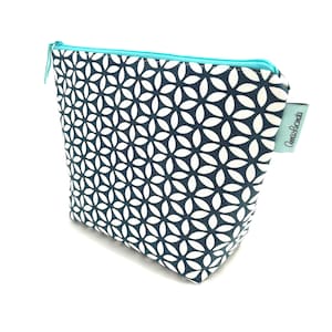May include: A navy and white floral patterned cosmetic bag with a turquoise zip. The bag has a rectangular shape with a slight taper. A small tag with the text "AnaLucinda" is attached to the side.