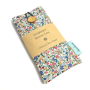 May include: A white fabric glasses case with a floral pattern in shades of pink, blue, and yellow. The case has a brown paper label that reads "Sunglasses/Glasses Case Made by Anna Lucinda" and a blue label that reads "Handmade".
