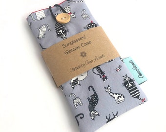 May include: A gray fabric sunglasses case with a black and white cat print. The case has a brown paper label that says "Sunglasses/Glasses Case" and "Made by Anna Lucinda".