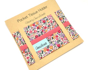May include: A brown cardboard package containing a floral fabric pocket tissue holder. The holder is made by Anna Lucinda and has a pink ribbon.