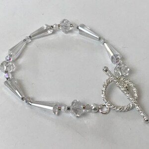 Pode incluir: Uma pulseira de prata com contas de cristal transparente e um fecho de correr de prata.