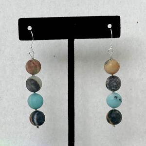 May include: A pair of dangle earrings with four round beads each. The beads are a mix of brown, black, and turquoise colors. The earrings are hanging from silver hooks.