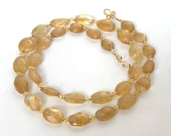 May include: A gold necklace with oval-shaped, light brown gemstones. The necklace is made of small, gold beads and has a clasp.