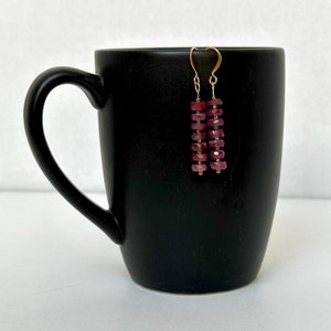 Op de afbeelding: Een paar gouden oorbellen met een rij roze facetgeslepen edelstenen.