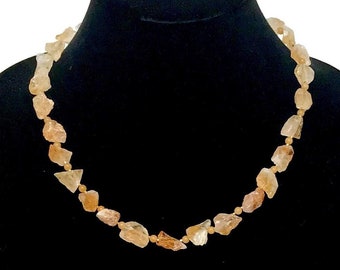 May include: A necklace made of light brown, irregular shaped stones on a black velvet display stand.