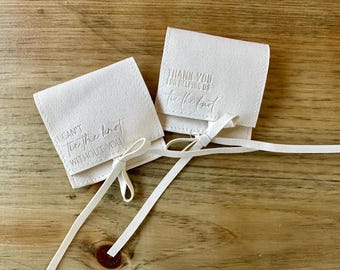 Könnte beinhalten: Zwei weiße Stoffgeschenktüten mit weißen Schleifenbändern. Eine Tasche sagt "Ich kann den Knoten nicht ohne dich binden" und die andere sagt "Danke, dass du uns beim Binden des Knotens geholfen hast".