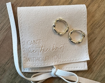 May include: A white suede pouch with a drawstring closure and the text "I can't tie the knot without you". The pouch contains two gold hoop earrings.