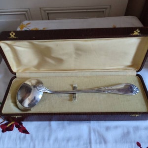 Peut inclure: Une louche de service en argent dans un coffret en cuir marron avec une doublure en velours jaune. La louche a un manche décoratif avec un motif floral.