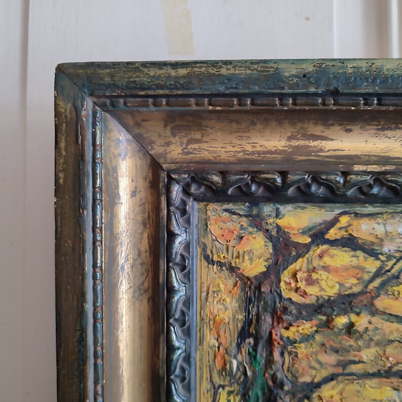 May include: Close-up of a gold-toned wooden frame with a dark green border. The frame surrounds a painting of a landscape with trees and foliage in shades of yellow, orange, and green.