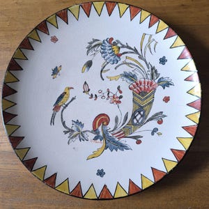 Puede incluir: Un plato de cerámica blanco con un diseño floral amarillo, rojo y azul. El plato tiene un borde festoneado con un borde amarillo y rojo.