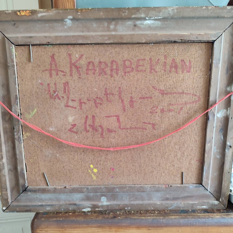 May include: The back of a framed painting with the artist's signature "A. Karapetkian" written in black ink. The signature is followed by a series of red lines and a red string.