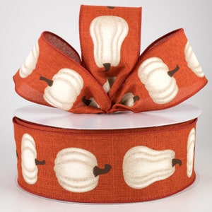 May include: A spool of 2.5 inch wide orange and white ribbon with a pumpkin print. The ribbon is made of a linen fabric and has a subtle texture.