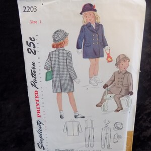 Könnte beinhalten: Simplicity Druckmuster 2203, Größe 1, für 25 Cent. Das Muster enthält Anleitungen zum Nähen eines Kindermantels und einer Hose. Das Bild zeigt drei Kinder, die die Kleidungsstücke tragen. Das Mädchen links trägt einen karierten Mantel, das Mädchen in der Mitte trägt einen blauen Mantel und der Junge rechts trägt einen braunen Mantel.
