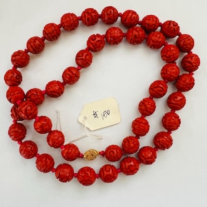 May include: A red carved bead necklace with a gold clasp. The beads are intricately carved with a floral design. A price tag is attached to the necklace.