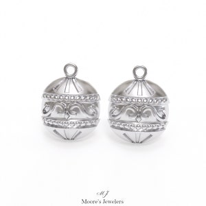 May include: A pair of silver ornament earrings with a detailed design. The ornaments are round and have a textured surface with a beaded border and a swirl pattern.