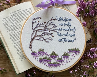 May include: An embroidered hoop art piece with the quote "Whatever our souls are made of, his and mine are the same." The design features a tree and lavender-colored floral accents. A book and flowers surround the hoop.