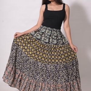 May include: A long, tiered skirt with a floral pattern in shades of black, yellow, blue, and pink. The skirt is paired with a black tank top. The skirt's design features multiple layers with a flowing, bohemian style.