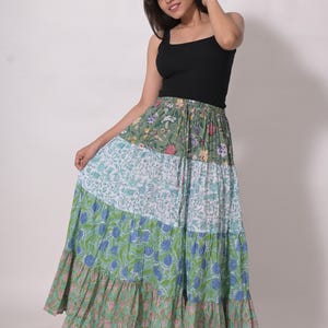 May include: A tiered maxi skirt with a floral print in shades of green, blue, and pink. The skirt is paired with a black tank top. The skirt's design features a mix of floral and leaf patterns.