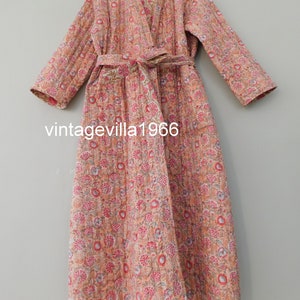 Könnte beinhalten: Eine lange, rosa-weiße Robe mit floralem Muster und einem passenden Gürtel. Die Robe ist gesteppt und hat einen Schalkragen.