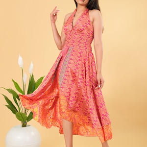 Puede incluir: Vestido halter rosa y naranja con un diseño geométrico. El vestido tiene un dobladillo asimétrico. La modelo lleva el vestido. Una planta en maceta blanca está a la izquierda sobre una estera tejida. El vestido mide unos 120 cm de largo.