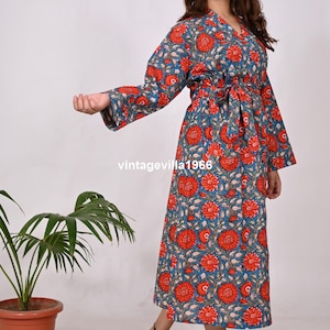 May include: A long, blue floral print robe with red flowers and green leaves. The robe has a V-neck, long sleeves, and a matching belt. The text "vintagevilla1966" is visible on the robe. The robe is knee-length.