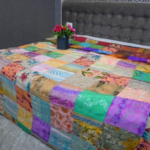 May include: A colorful patchwork quilt made from various fabrics in shades of pink, purple, green, blue, and brown. The quilt is made up of squares of different sizes and patterns, creating a unique and eye-catching design.