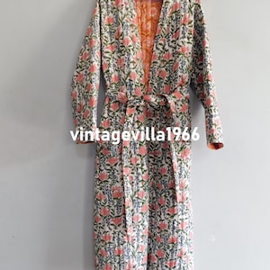 May include: A long white robe with a floral print in shades of pink, green, and blue. The robe has a tie belt and a V-neck.