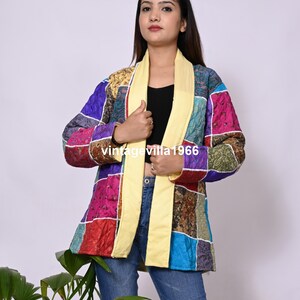 May include: A colourful patchwork jacket with a yellow collar and a quilted design. The jacket is made of different fabrics and has a variety of colours, including purple, blue, green, and pink.