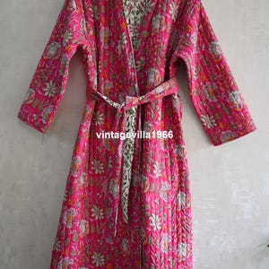 May include: A quilted pink robe with a floral pattern and a matching belt. The robe is reversible, with a cream-colored floral pattern on the inside. The text "vintagevilla1966" is printed on the belt.