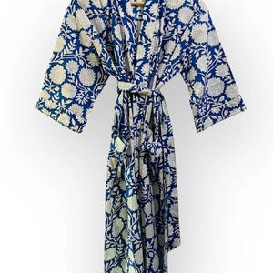 May include: A blue and white floral print robe hanging on a wooden hanger. The robe features a repeating pattern of white flowers and leaves against a deep blue background. It has a matching belt and pockets.