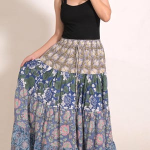 Puede incluir: Una falda larga de capas con cintura de cordón y un estampado floral multicolor hecho con bloques. La falda se compone de cuatro paneles horizontales distintos, cada uno con diferentes motivos botánicos en tonos de azul, verde y rosa.