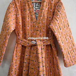 May include: An orange quilted robe with a floral pattern and a matching belt. The robe has a V-neck and long sleeves. The interior lining features a contrasting floral print. The text "vintagevilla1966" is visible on the belt.