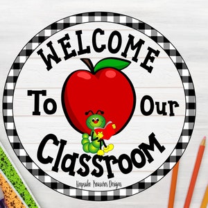May include: A round classroom sign with a black and white checkered border. The sign features the words "WELCOME To Our Classroom" in black text. A red apple with a green leaf and a cartoon caterpillar reading a book are in the center.