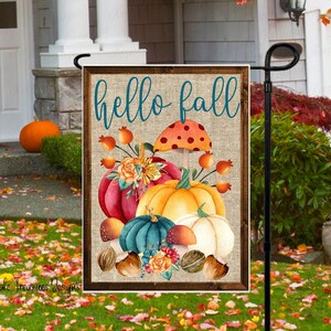 Może przedstawiać: Flaga ogrodowa z płótna jutowego z drewnianą ramą zawiera napis "hello fall" w niebieskim stylu pisma. Flaga jest ozdobiona akwarelową ilustracją dyni, grzybów i jesiennych liści.