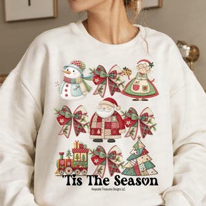 Puede incluir: Sudadera blanca con gráficos navideños coloridos. El diseño incluye un muñeco de nieve, Papá Noel, lazos, un tren y un árbol de Navidad. El texto "Tis The Season" está impreso en la parte inferior.