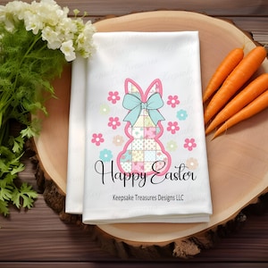 以下が含まれることがあります： 白地にパッチワークのウサギのデザインとピンクとブルーの文字で「Happy Easter」と書かれた白いキッチンタオル。ウサギは青いリボンをつけており、ピンクとブルーの花に囲まれています。