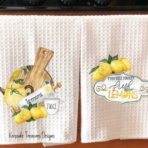 May include: Two white kitchen towels with lemon designs. The first towel features a wooden cutting board, a teapot, a lemon juicer, and lemons. The second towel features a sign that says "Farmers Market Fresh Lemons".