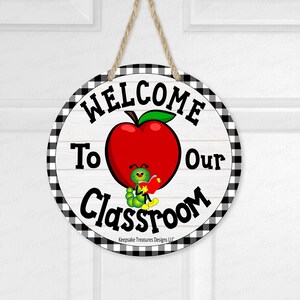May include: Round wooden sign with a black and white checkered border. The sign reads "WELCOME To Our Classroom" with a red apple and a cartoon caterpillar holding a book. A jute rope is attached for hanging.