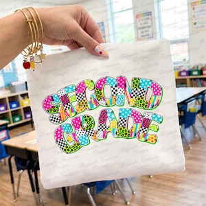 Peut inclure: Un t-shirt blanc avec le texte SECOND GRADE en grandes lettres grasses de style bulle. Chaque lettre est remplie d'un motif vibrant et multicolore incluant des étoiles, des taches de léopard et des carreaux en rose, vert et bleu vifs.
