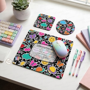 May include: A black composition notebook-themed mousepad, coaster, and square coaster set with colorful graphics of cherries, butterflies, and smiley faces. The mousepad measures 9.75 x 7.3 inches. A rainbow-colored mouse and keyboard are also visible.